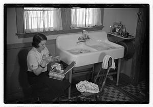 A woman sewing next to a sink full of laundry