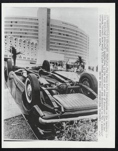 The famous Hotel Fontainebleau is the backdrop for this overturned auto, left upside down by the wind and water of Hurricane Cleo on her passage through here early 8/27. The fabled vacationland was described as "in a shambles" after Cleo moved north.