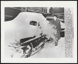 New York - Driver's Dilemma - J.A. O'Neill of Baltimore, Md., in New York City on a short vacation, scrapes snow off top of his car this morning after he had left it parked out overnight on West 51st Street in midtown Manhattan. Mrs. O'Neill peers out of windshield through tunnel-like opening cleared in a foot of snow which fell overnight. Storm was Manhattan's worst in seven years.