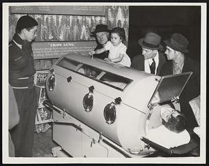 Iron Lung Displayed in Station. The Iron Lung set up in Illinois Central Randolph Street station here to receive donations for the infantile paralysis fund. Photo shows contributions being made through a hole in the top of the lung. The equipment is in operation with a wax model inside.