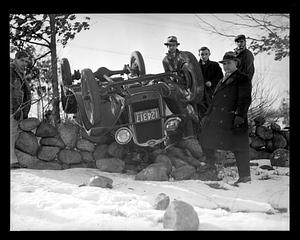 Spectators pose by an overturned car