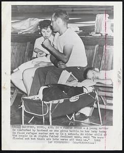 Family Scene- A young mother is comforted by husband as she gives bottle to her baby today in flood refugee center set up in a school, An older child of the couple is at right. Father declined name, said "We were flooded out but there are lots worse off than us." 1955.