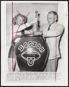 Prize Jug--Baton twirler Dottie Grover and Coach Ben Schwartzwalder of the Syracuse University football team try to stir up a victory potion today in the bean pot trophy that will be at stake Friday night when Syracuse and Boston University teams clash here.