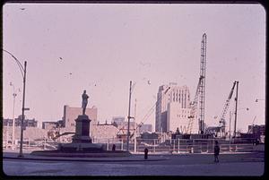 Cranes in front of buildings, Samuel Adams statue in foreground