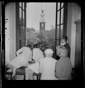 People looking out a window to see Harvard Commencement, with the bell tower of Memorial Church in the distance