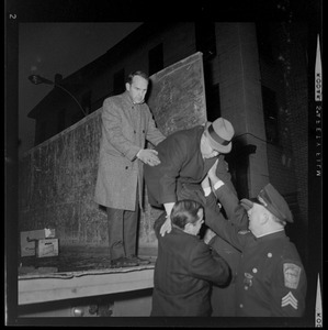 Unidentified man being assisted climbding out of a truck by two men and police officer