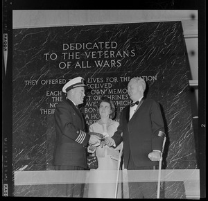 Navy captain with Mary Collins and Mayor John F. Collins in front of plaque wall dedicated to veterans of all wars