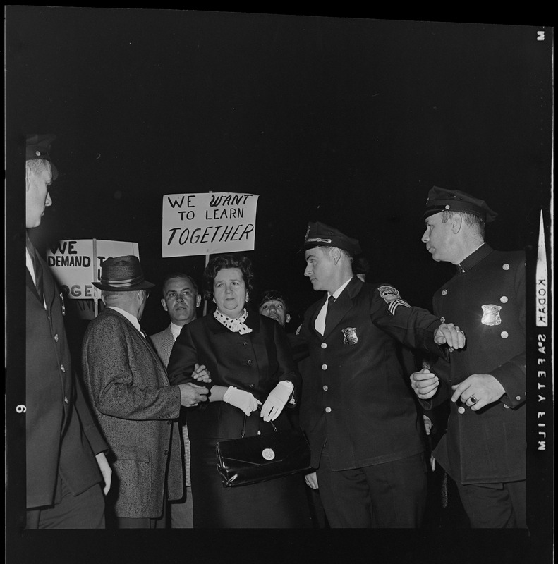 Louise Day Hicks escorted by Sgt. John Hames and unidentified police officers through protest against school segregation outside Boston School Committee meeting