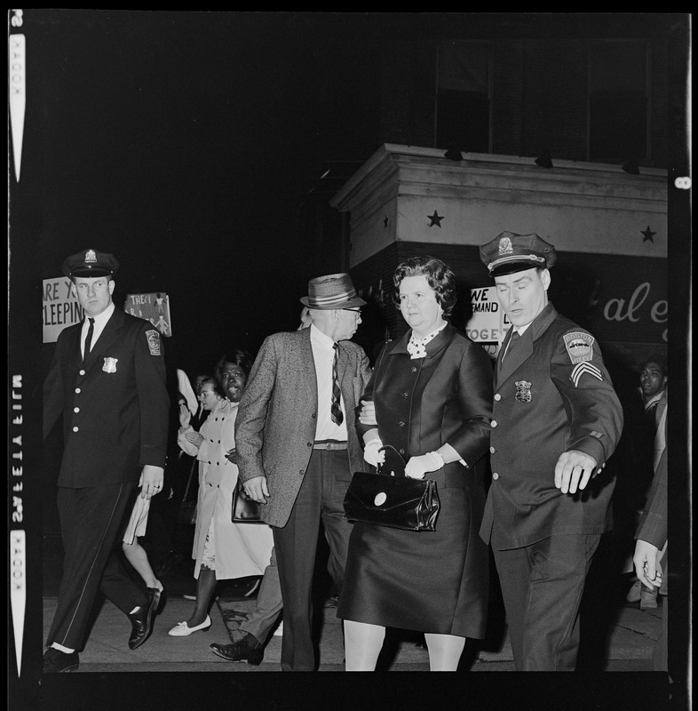 Louise Day Hicks escorted by Sgt. John Hames and unidentified police officers through protest against school segregation outside Boston School Committee meeting
