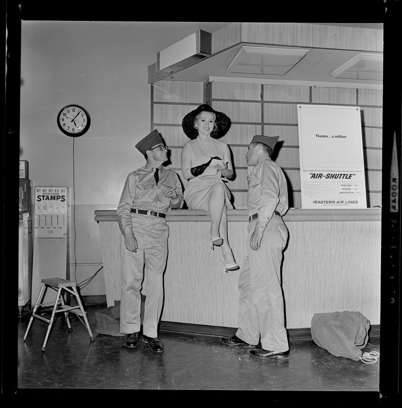 Film actress Zsa Zsa Gabor makes herself comfortable at Logan Airport after arriving in Boston for visit. First to spot her were GIs Steven Weiner, Dorchester and Stephen Avslander, Brookline, who wait as Zsa Zsa gives her autograph