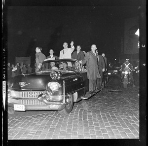 President Johnson and Lt. Gov. Bellotti, surrounded by Secret Service men, wave to crowds as they ride in motorcade from Logan Airport