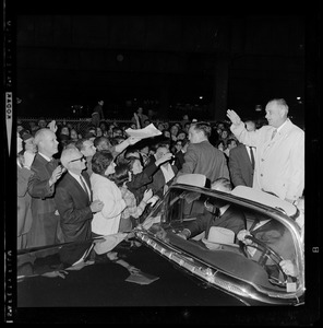 President Johnson, surrounded by Secret Service men, waves to crowds as he rides in motorcade from Logan Airport