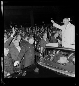 President Johnson, surrounded by Secret Service men, waves to crowds as he rides in motorcade from Logan Airport