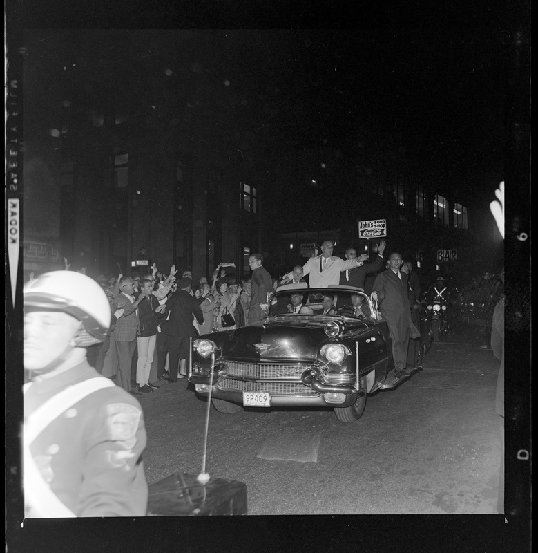 President Johnson and Lt. Gov. Bellotti, surrounded by Secret Service men, wave to crowds as they ride in motorcade from Logan Airport