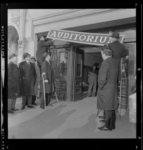 Men hanging "Auditorium" sign over doorway at War Memorial Auditorium as Mayor John Collins watches
