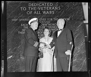 Navy captain with Mary Collins and Mayor John F. Collins in front of plaque wall dedicated to veterans of all wars