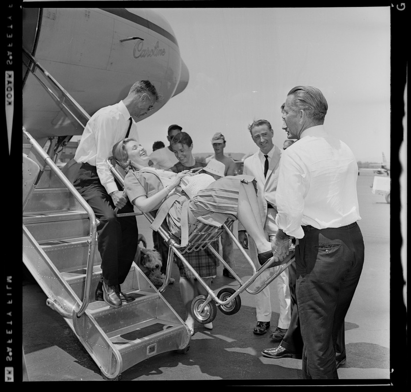 Marvella Hern Bayh in upright stretcher being carried onto the Kennedy family plane "Caroline"