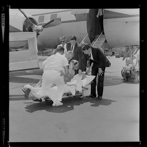 Orderlies lifting Marvella Hern Bayh from stretcher in front of the Kennedy family plane "Caroline," with Sen. Birch Bayh