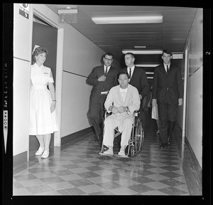 Student nurse Wendy Cowles pauses in her work to watch Sen. Bayh--confined to wheelchair, he's pushed by Dr. David Jackson to press session