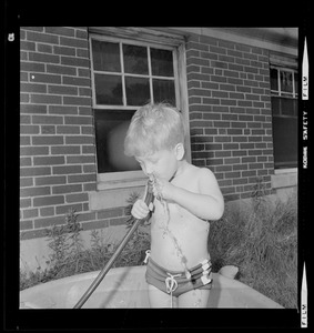 Child drinking from a hose while playing in a wading pool