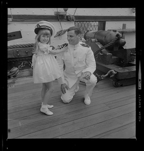 Tufts Naval ROTC graduate kneeling on deck of Old Ironsides with young girl wearing sailor's cap