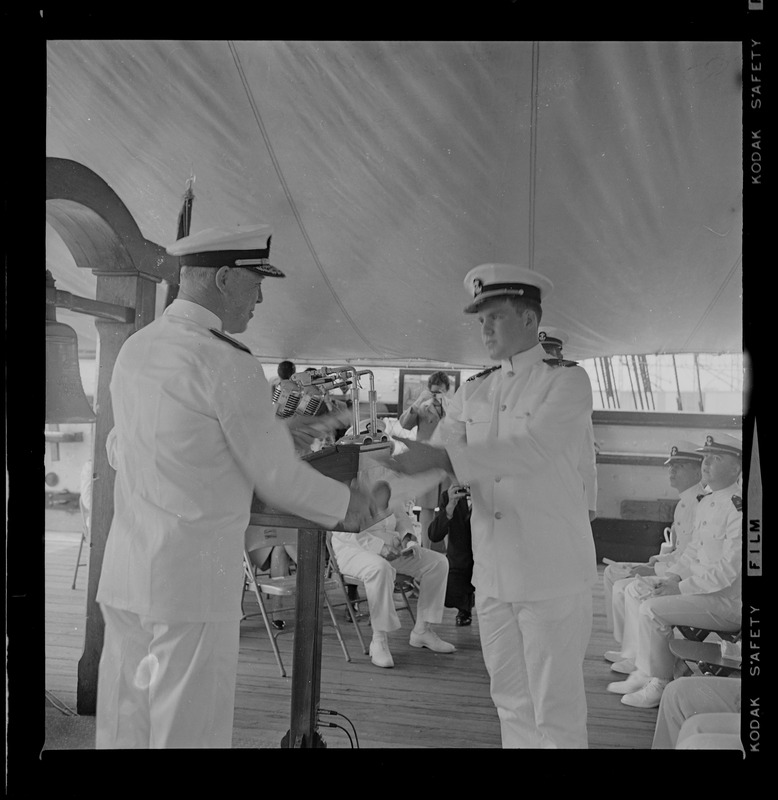 Rear Admiral Joseph C. Wylie shaking hands and presenting diploma to Naval ROTC graduate at commissioning ceremony aboard Old Ironsides