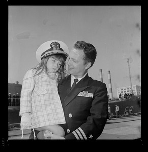 Navy commander holding little girl at departure of USS Boston from South Boston Naval Annex for tour of duty in Vietnam