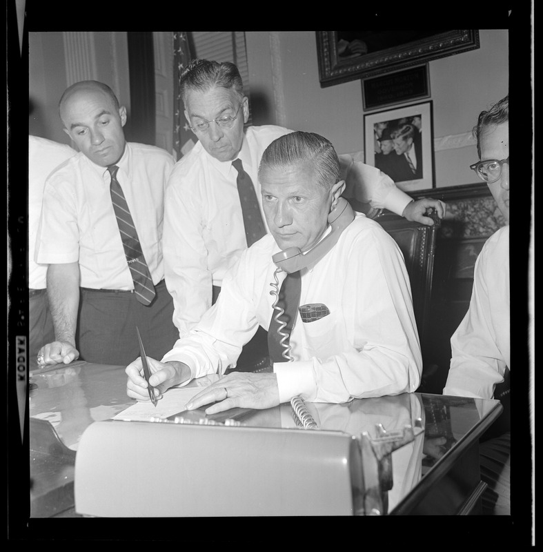 Gov. John A. Volpe, on phone at the State House, checks conditions in Springfield as aides Joseph Tauro, Timothy Regan, and Lt. Gov. Elliott Richardson stand by