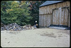 Woodpile and costumed woman next to barn, Old Sturbridge Village, Sturbridge, Massachusetts