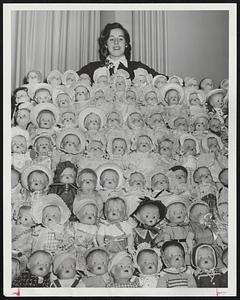 Happiness for Hundreds of little girls will come from the 230 dolls which have been dressed by woman employes of the Federal Reserve Bank of Boston, for distribution to needy children. Miss Janice Jacobs poses wit some of the dolls.