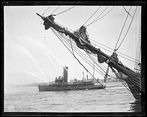 The prow of a sailing ship in foreground, a fireboat in the background