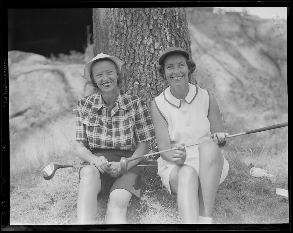 Two women golfers rest on tree