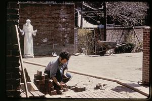 A man laying brick in the courtyard of the Old North Church, statue of St. Francis of Assisi in the background