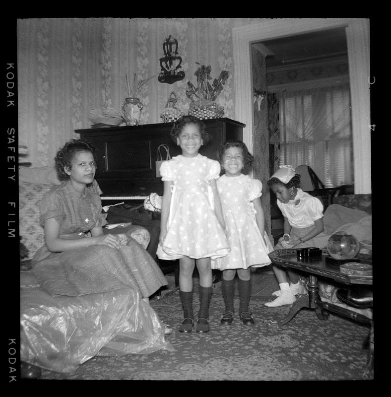 Two girls stand, one woman and one girl sit