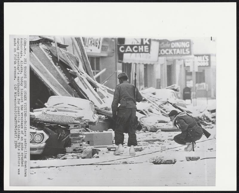 Troops Seek Quake Victims--Soldiers patrolling downtown Anchorage, Alaska, today inspect the wreckage of an auto crushed during yesterday's earthquake for possible victims. This picture was made on Fifth avenue.