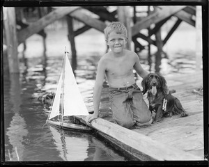 Boy and his dog play with toy sailboat