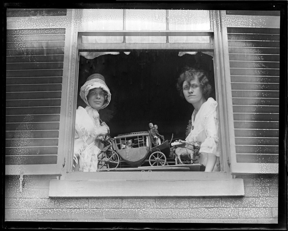Ladies in costume pose in window with toy carriage (possibly Beacon Hill)