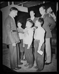 Boys' Clubs of Boston members receive Victory Volunteers badges from Pfc. Hy Rosen while Col. George A. Ford and Frederic C. Church, Jr., watch at Jordan Marsh Co. Auditorium