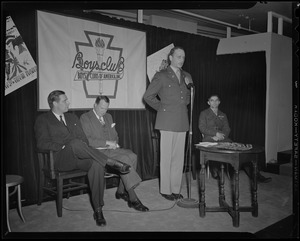 Col. George A. Ford speaks at induction of Boys' Club of Boston members into the Victory Volunteers while Boston Mayor Maurice Tobin, Frederic C. Church, Jr., and Pfc. Hy Rosen watch at Jordan Marsh Co. Auditorium