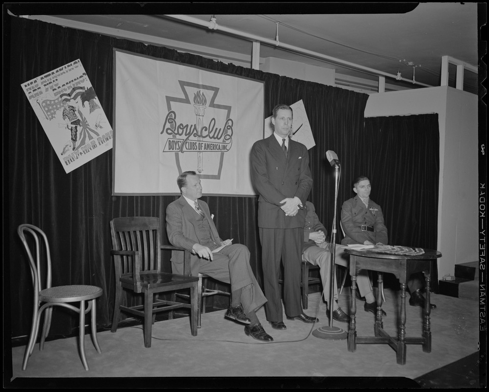 Boston Mayor Maurice Tobin speaks at induction of Boys' Club of Boston members into the Victory Volunteers while Frederic C. Church, Jr., Col. George A. Ford, and Pfc. Hy Rosen watch at Jordan Marsh Co. Auditorium