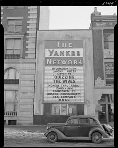 Street scene with Yankee Network letter board sign advertising Quizzing the Wives on WNAC sponsored by Boston Consolidated Gas Company