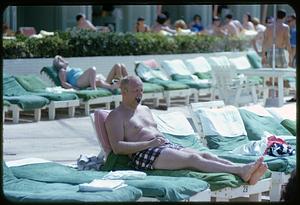 Man smoking pipe in lounge chair in pool or beach area, Eden Roc Hotel, Miami Beach, Florida