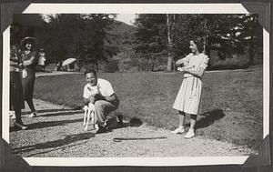 An unidentified man holding a goat, two unidentified women standing to the side