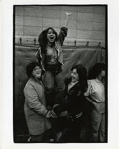 Two teenage girls hold up a third cheering teenage girl