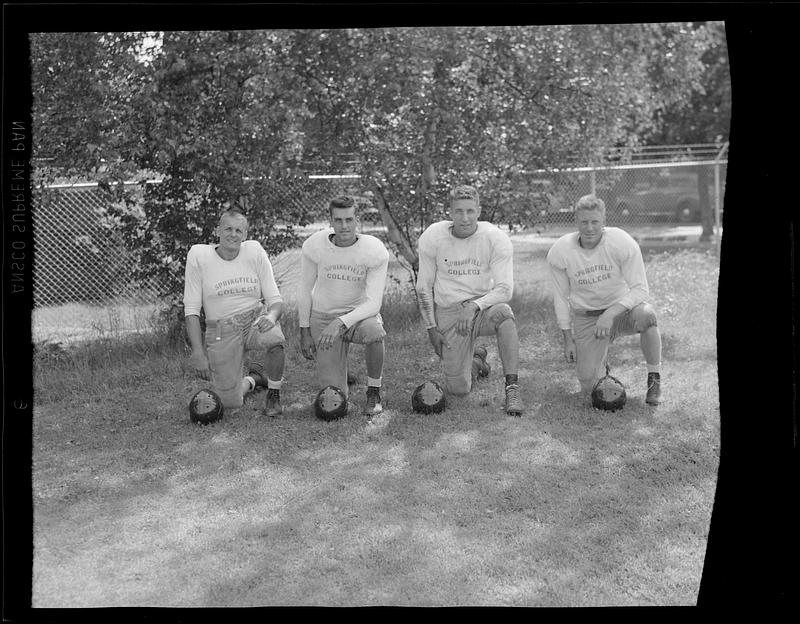 Four football players kneel with their helmets