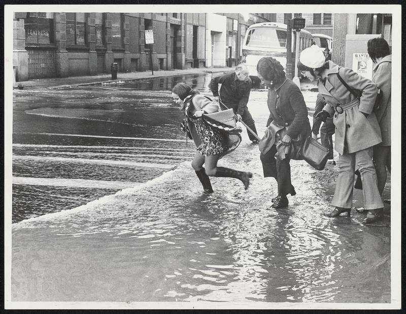 Women Learned quickly whether their high boots were waterproof yesterday when they attempted to ford this stream caused by a water main break at downtown South and Essex streets.