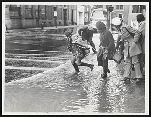 Women Learned quickly whether their high boots were waterproof yesterday when they attempted to ford this stream caused by a water main break at downtown South and Essex streets.