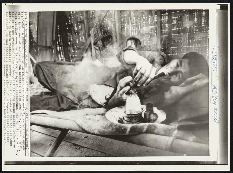 Problems Go Up in Smoke-A man contentedly smokes his opium pipe in corner of American run hospital at Ban Son, Laos, as small girl, just visible over man's elbow, plays in background. The man is a civilian, one of those evacuated from a hospital at Long Cheng shortly before an attack by North Vietnamese troops. Like thousands of Meo and Lao Tung tribesmen, he has joined a growing flood of refugees fleeing before [illegible]