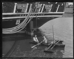 Boys in outrigger paddle under stern of the USS Constitution