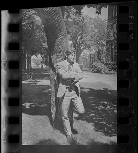 Man with camera leaning against a tree on Tufts University campus